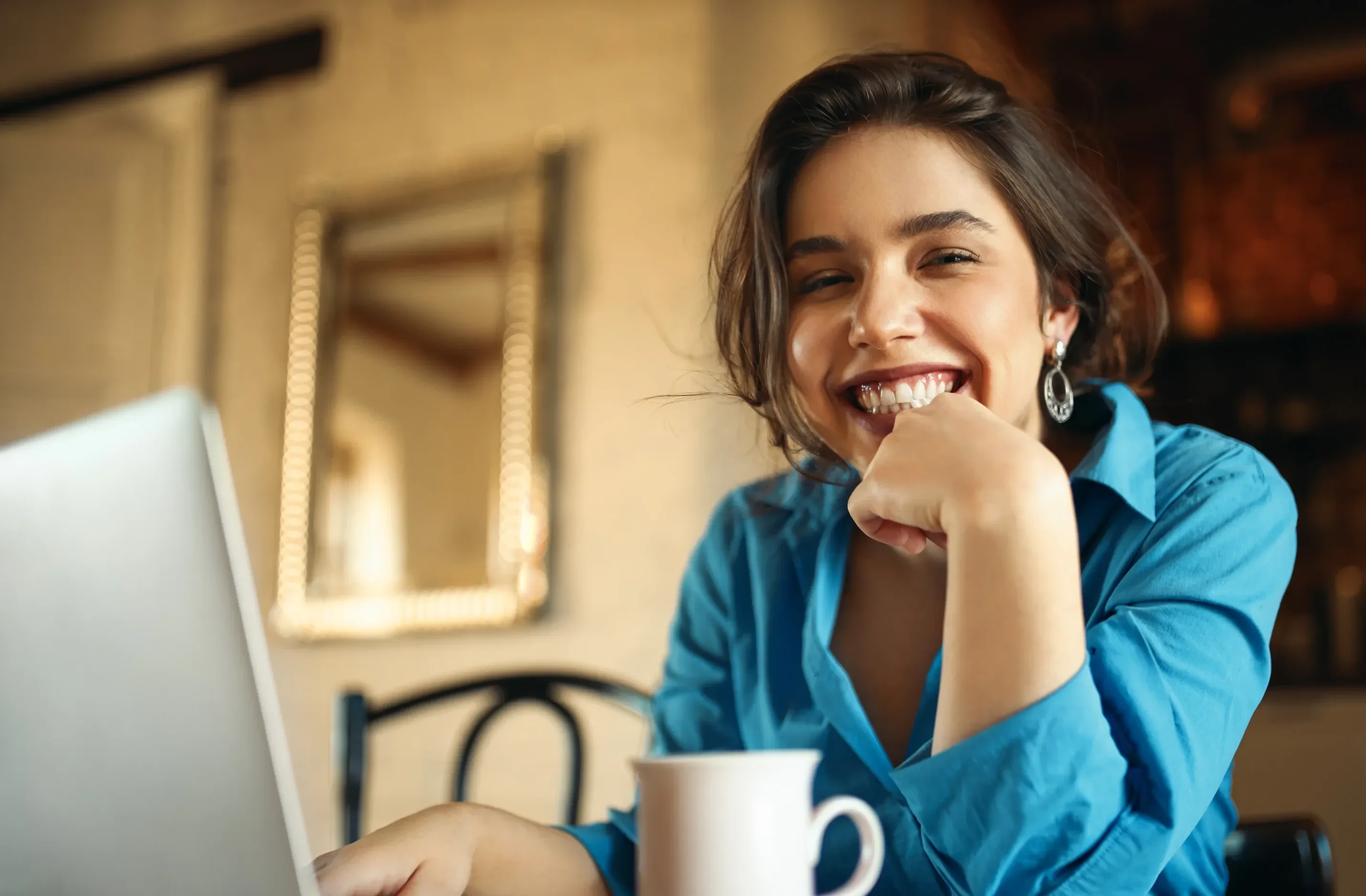 Mulher sorrindo em um café, trabalhando no notebook com uma xícara ao lado