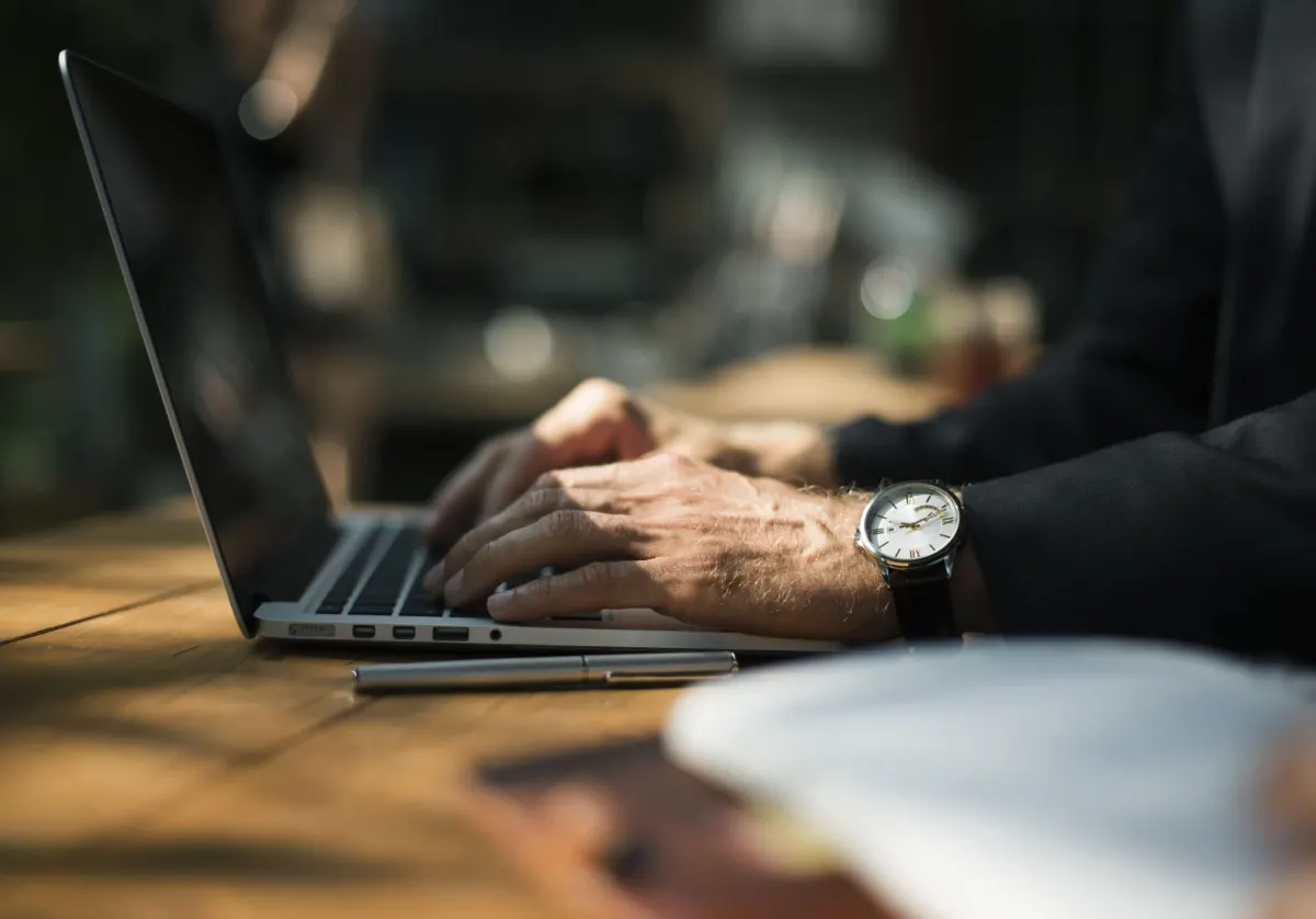 Mãos digitando em um notebook sobre uma mesa de madeira